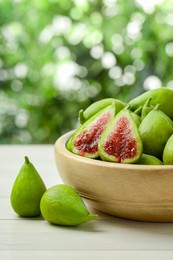 Photo of Cut and whole fresh green figs on white wooden table against blurred background, space for text