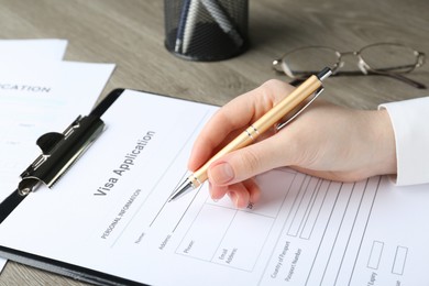 Woman filling visa application form for immigration at table, closeup