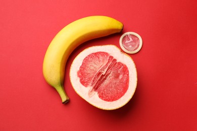 Banana, half of grapefruit and condom on red background, flat lay. Safe sex concept