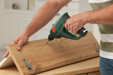 Man with electric screwdriver assembling furniture at table indoors, closeup