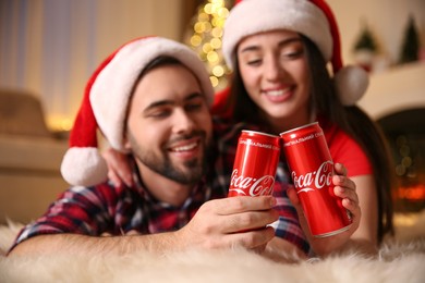 MYKOLAIV, UKRAINE - JANUARY 27, 2021: Young couple holding cans of Coca-Cola at home, focus on hands. Christmas atmosphere