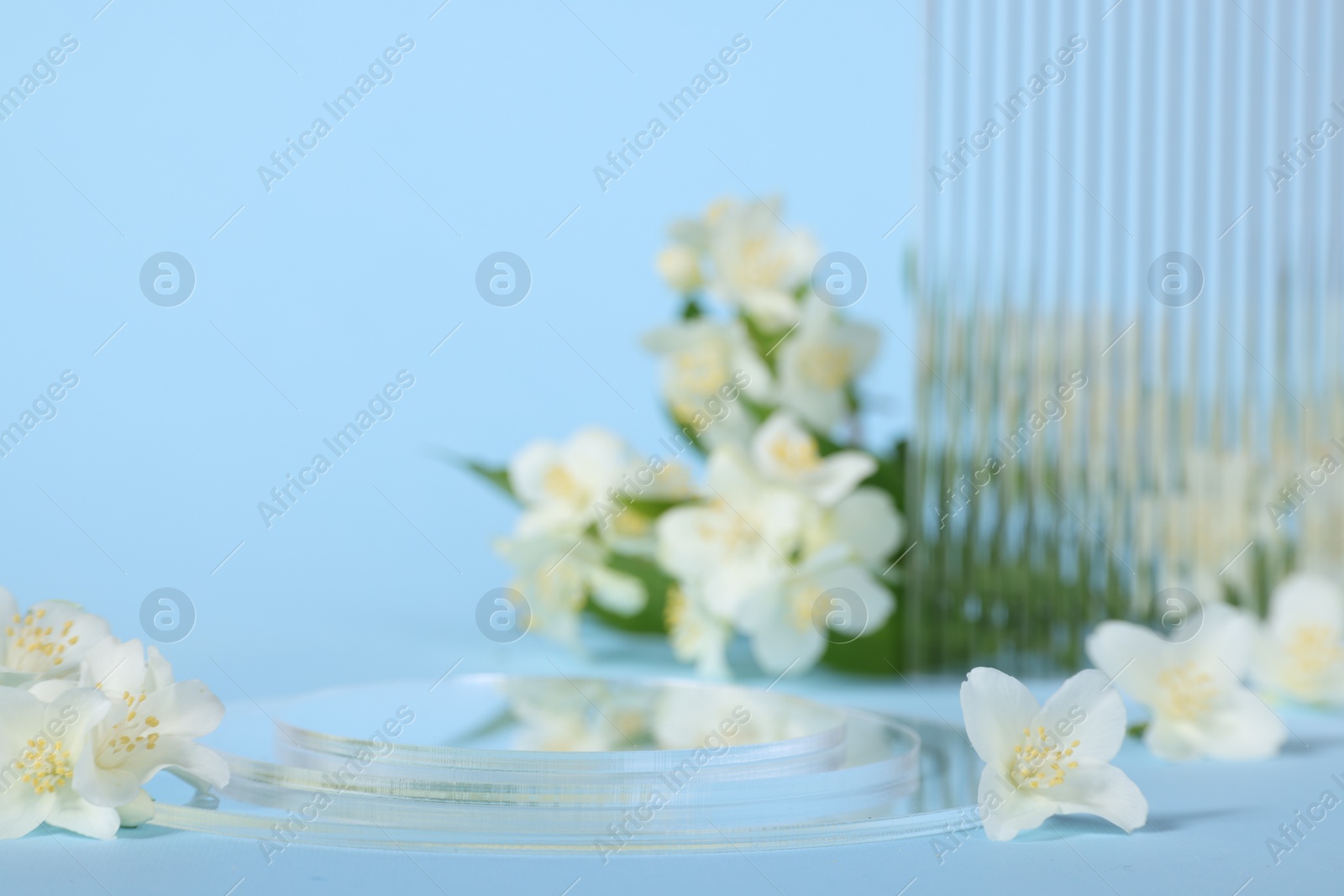 Photo of Presentation of product. Glass podium and beautiful jasmine flowers on light blue background, space for text