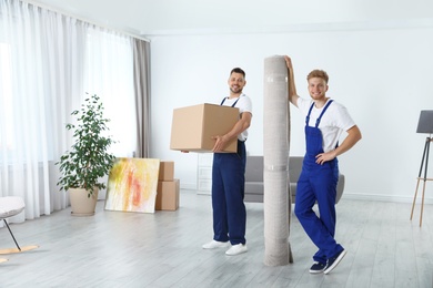 Moving service employees with box and carpet in room