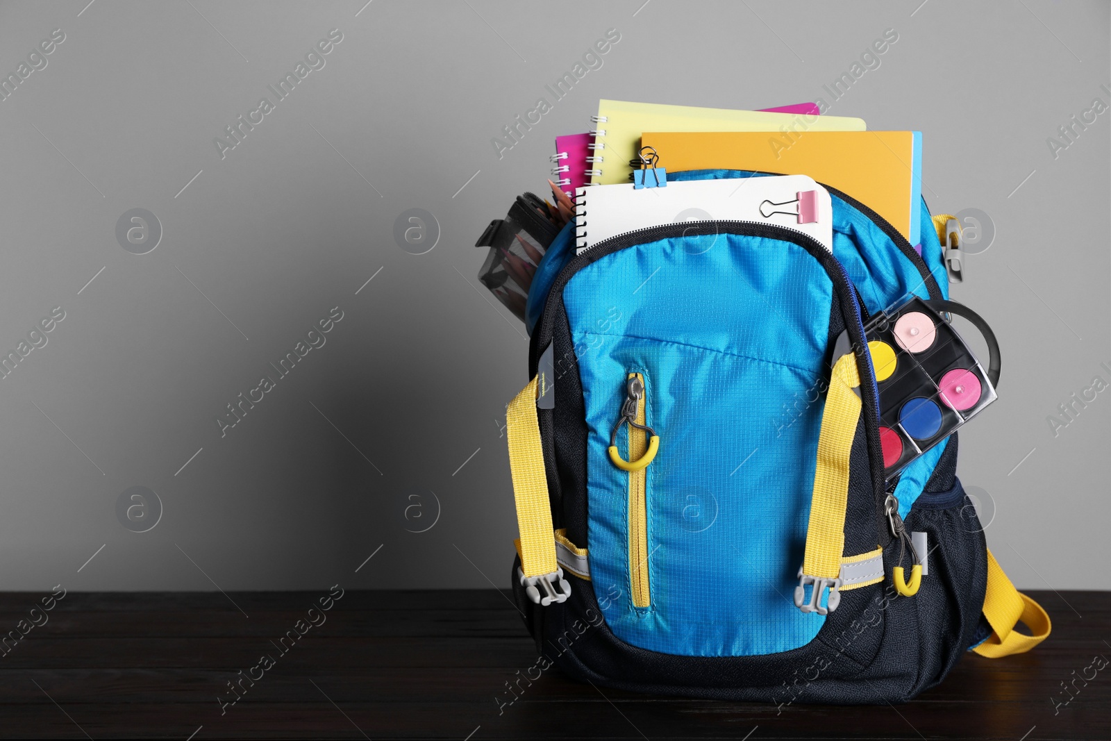 Photo of Children's backpack with different school stationery on wooden table against grey background, space for text