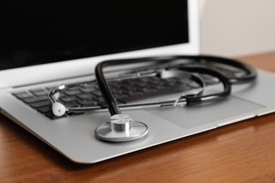 Photo of Modern laptop with stethoscope on wooden table, closeup