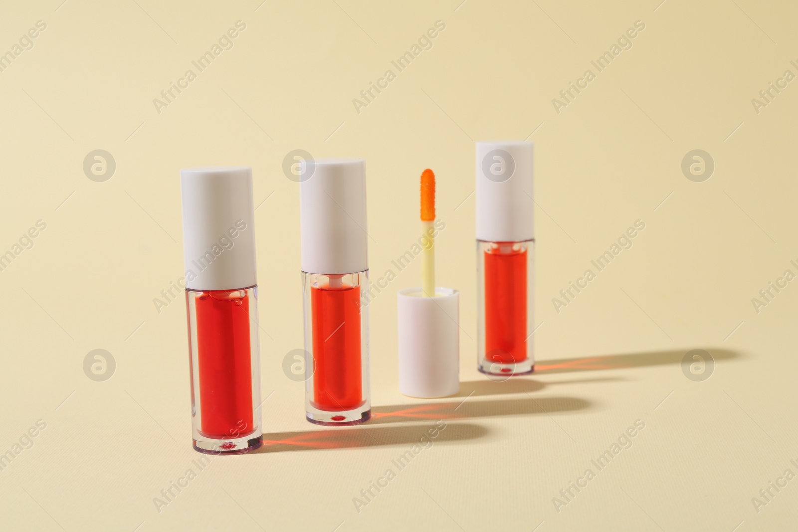 Photo of Bright lip glosses and applicator on beige background