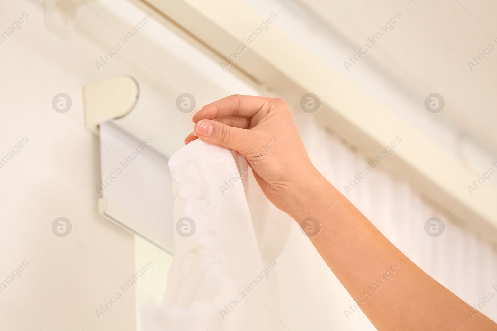 Photo of Young woman hanging window curtain in room, closeup
