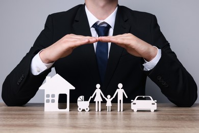 Photo of Man protecting figures of family, car and house at wooden table. closeup. Insurance concept
