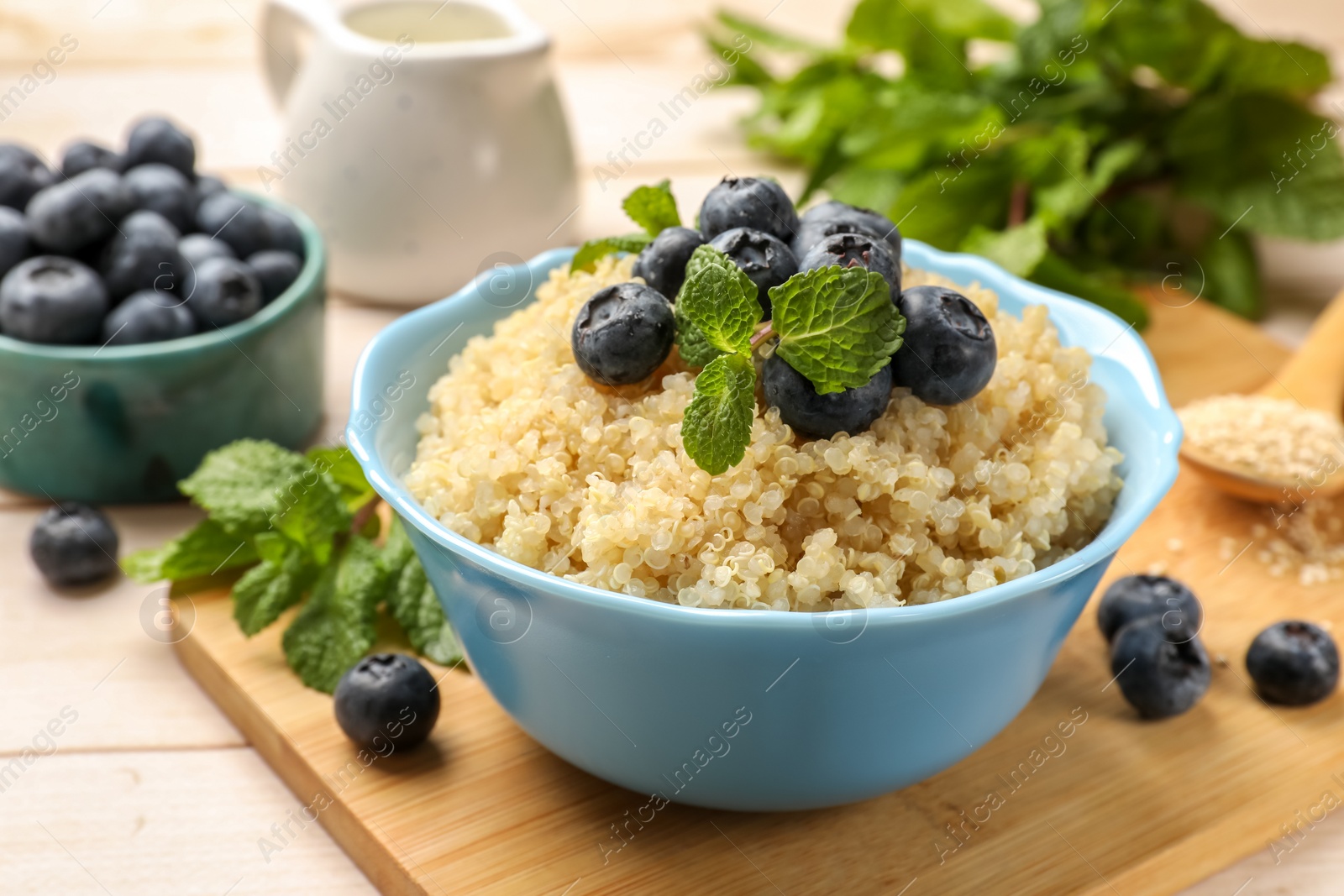 Photo of Tasty quinoa porridge with blueberries and mint in bowl on light table, closeup