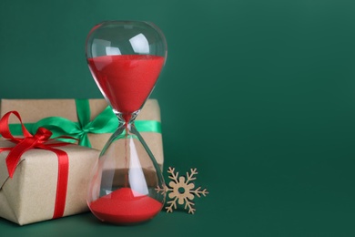 Photo of Hourglass and gifts on green background, space for text. Christmas countdown