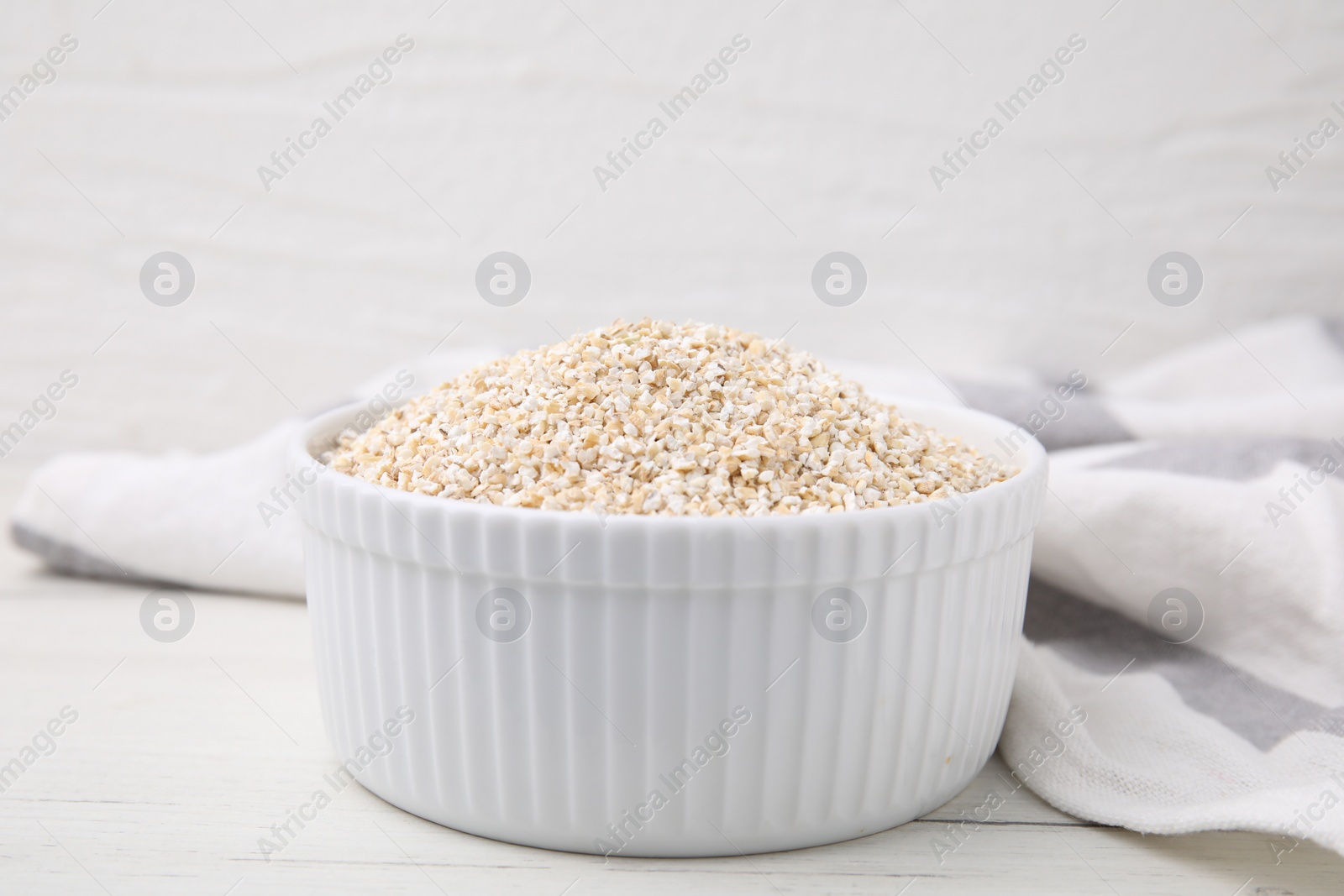 Photo of Dry barley groats in bowl on white wooden table, closeup