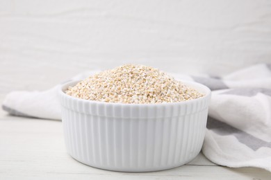 Photo of Dry barley groats in bowl on white wooden table, closeup