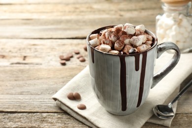 Photo of Delicious hot chocolate with marshmallows and cocoa powder in cup on wooden table, space for text