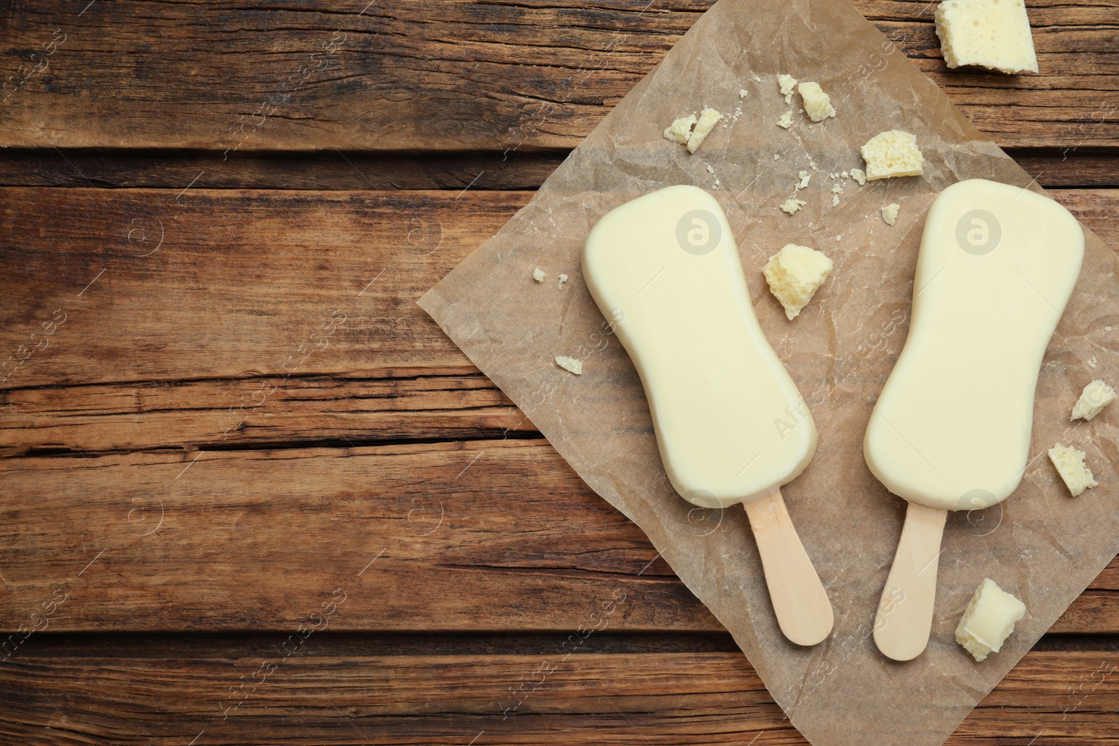 Photo of Glazed ice cream bars and white chocolate chunks on wooden table, flat lay. Space for text