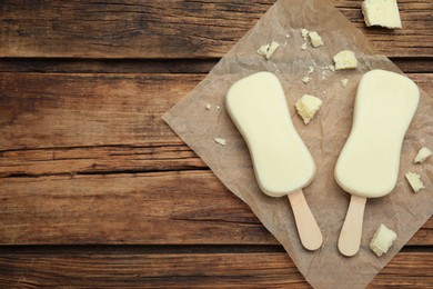 Photo of Glazed ice cream bars and white chocolate chunks on wooden table, flat lay. Space for text