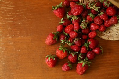 Photo of Basket with scattered ripe strawberries on wooden table, top view. Space for text