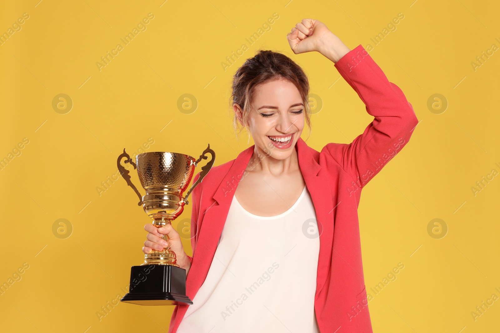 Photo of Portrait of happy young businesswoman with gold trophy cup on yellow background