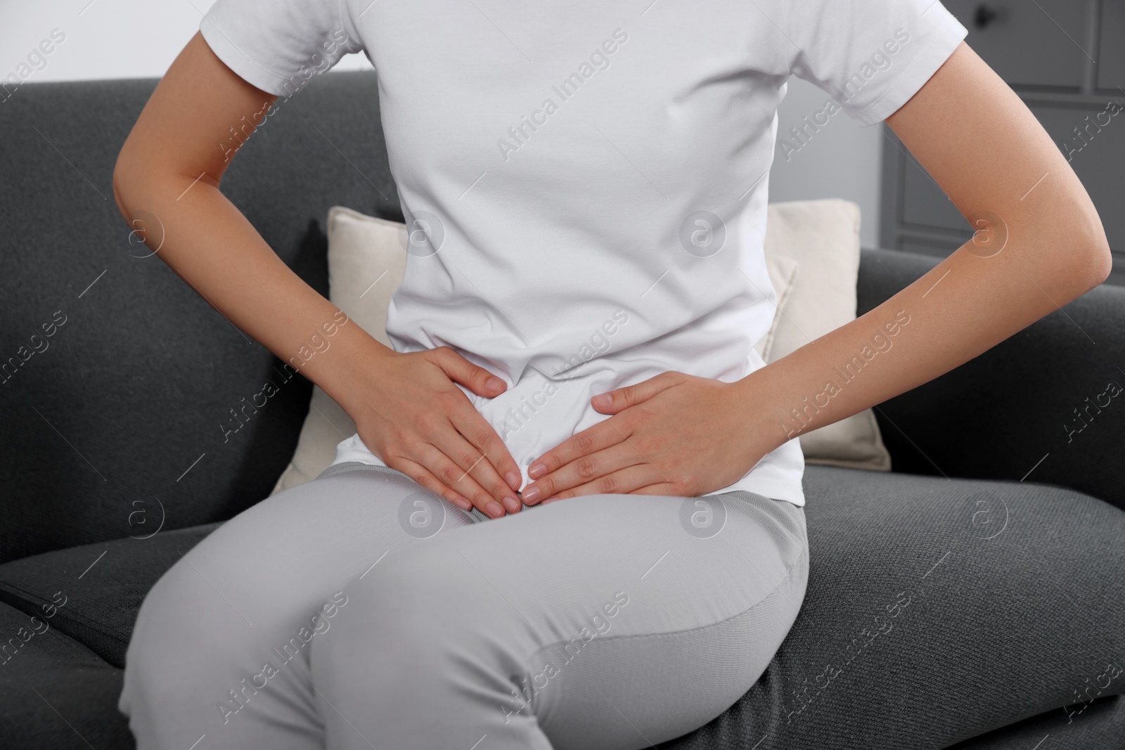 Photo of Woman suffering from cystitis on sofa at home, closeup