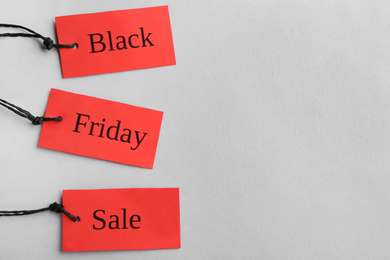 Red tags with words BLACK FRIDAY SALE on light background, top view