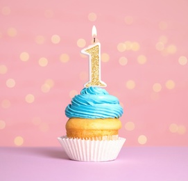 Photo of Birthday cupcake with number one candle on table against festive lights