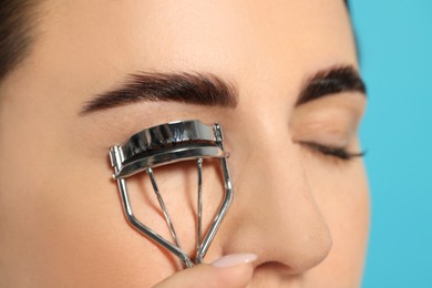 Photo of Woman using eyelash curler on turquoise background, closeup