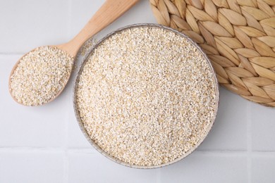 Photo of Raw barley groats in bowl and spoon on light tiled table, top view