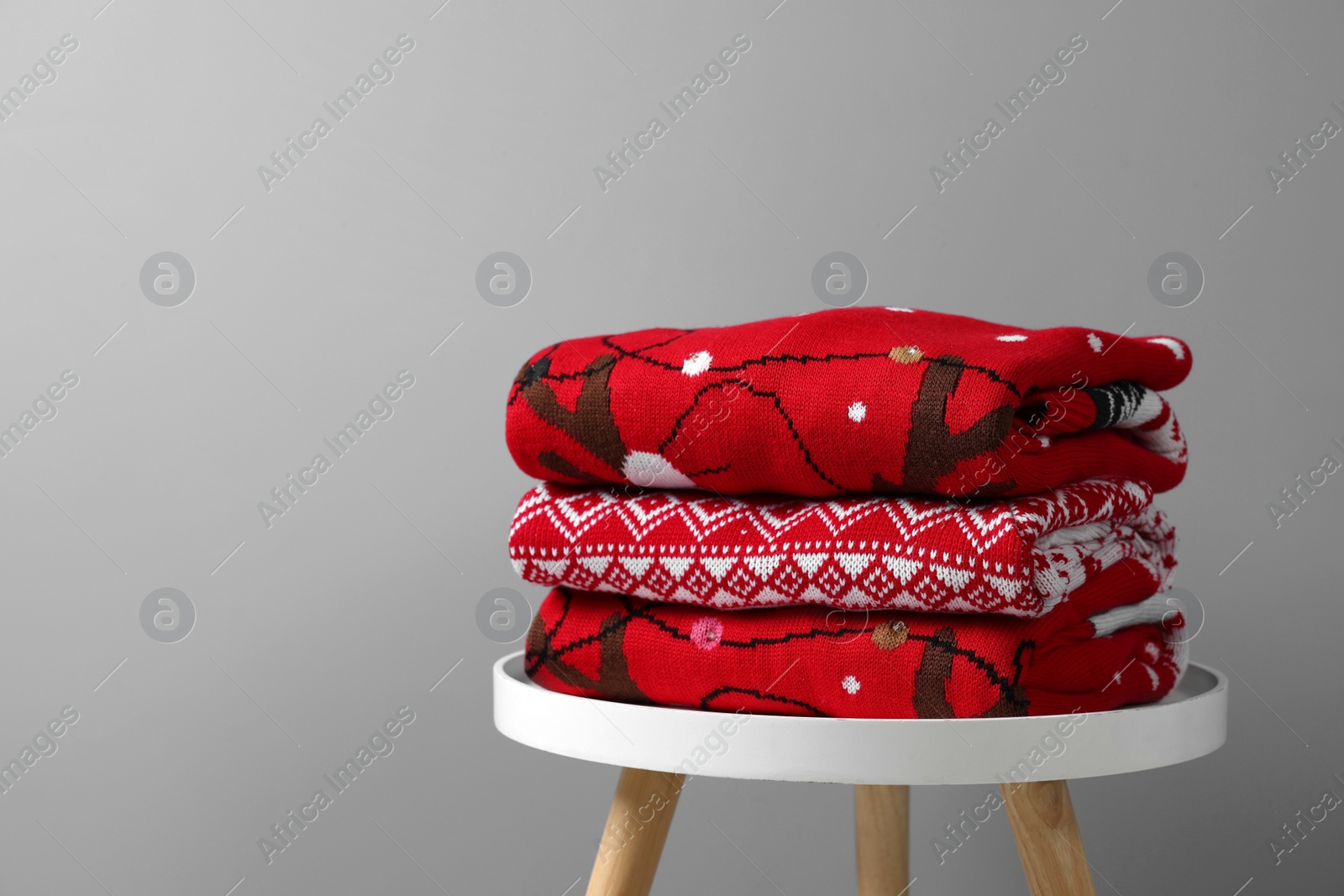 Photo of Stack of different Christmas sweaters on white table against grey background. Space for text