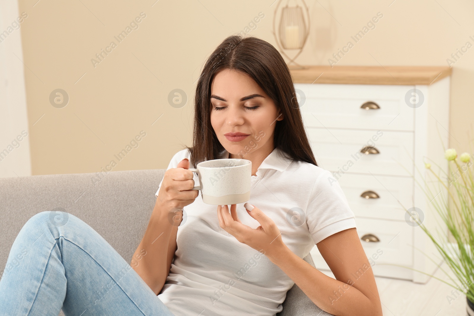 Photo of Beautiful woman with cup sitting on sofa at home