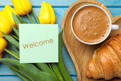 Image of Welcome card, beautiful yellow tulips, croissant and cup of aromatic coffee on light blue wooden table, flat lay