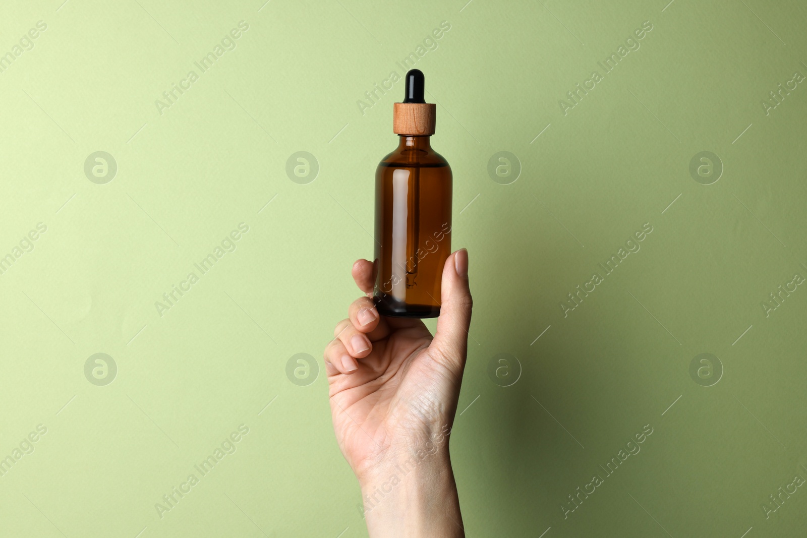 Photo of Woman holding bottle of cosmetic product on pale olive background, closeup. Space for text