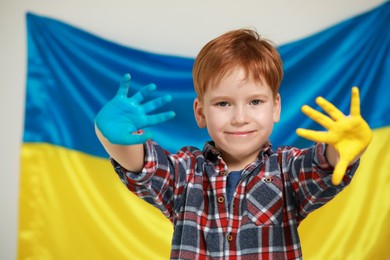 Photo of Little boy with painted hands near Ukrainian flag. Love Ukraine concept