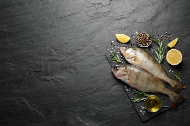 Photo of Fresh raw perches and ingredients on black slate table, flat lay with space for text. River fish