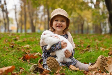 Girl sitting with cute white rabbit on grass in autumn park
