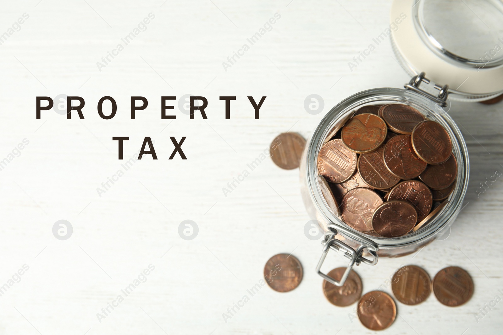 Image of Text Property Tax near jar full of coins on white wooden table, top view