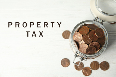 Text Property Tax near jar full of coins on white wooden table, top view