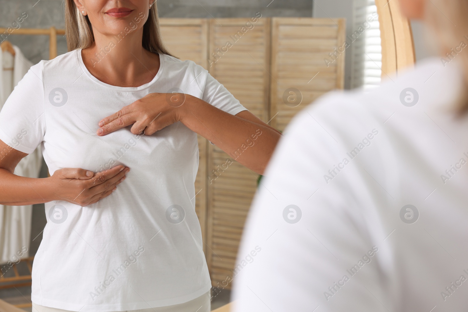Photo of Woman doing breast self-examination near mirror in bathroom, closeup