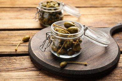 Tasty capers in glass jars on wooden table