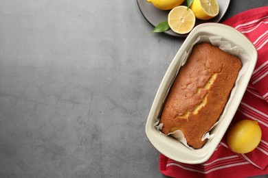 Photo of Tasty lemon cake in baking dish and citrus fruits on grey table, flat lay. Space for text