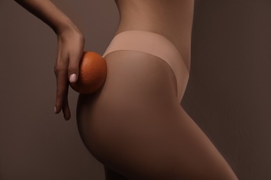 Closeup view of slim woman in underwear with orange on beige background. Cellulite problem concept