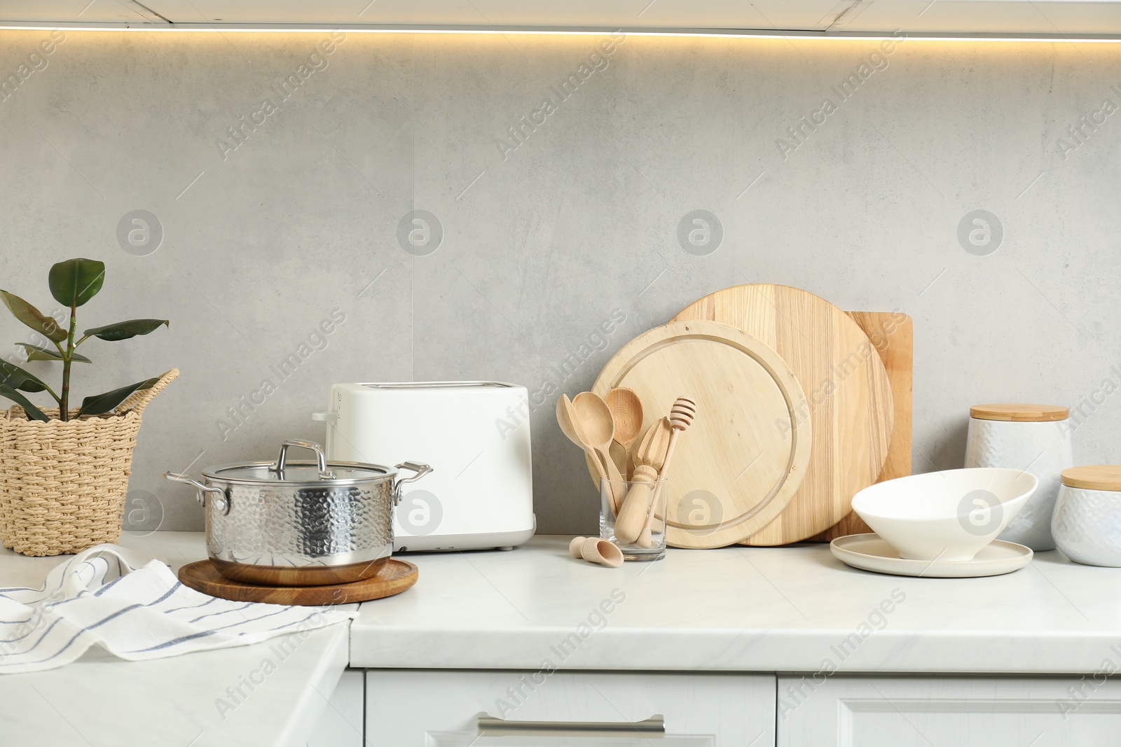 Photo of Different wooden cutting boards, toaster and other cooking utensils on white countertop in kitchen