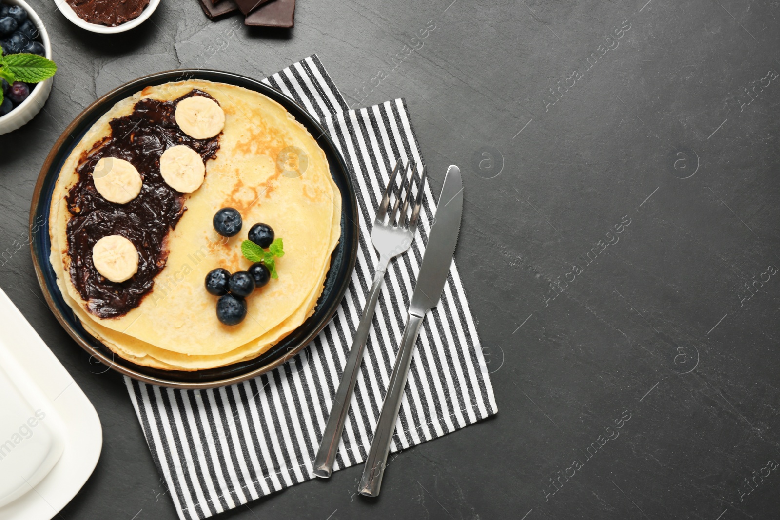 Photo of Delicious crepes with banana, blueberries and mint served on grey table, flat lay. Space for text