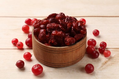 Photo of Dried cranberries in bowl and fresh berries on wooden table, closeup
