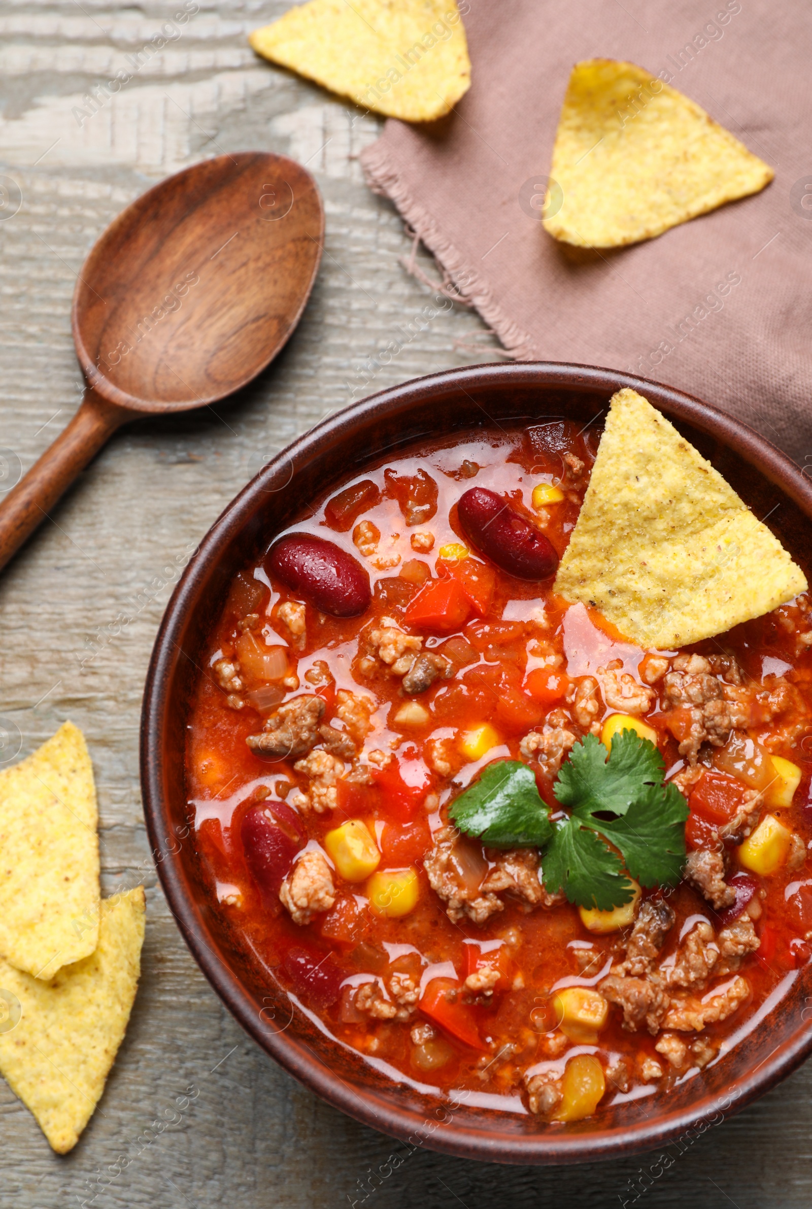 Photo of Tasty chili con carne with nachos served on wooden table, flat lay