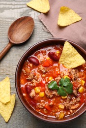 Tasty chili con carne with nachos served on wooden table, flat lay