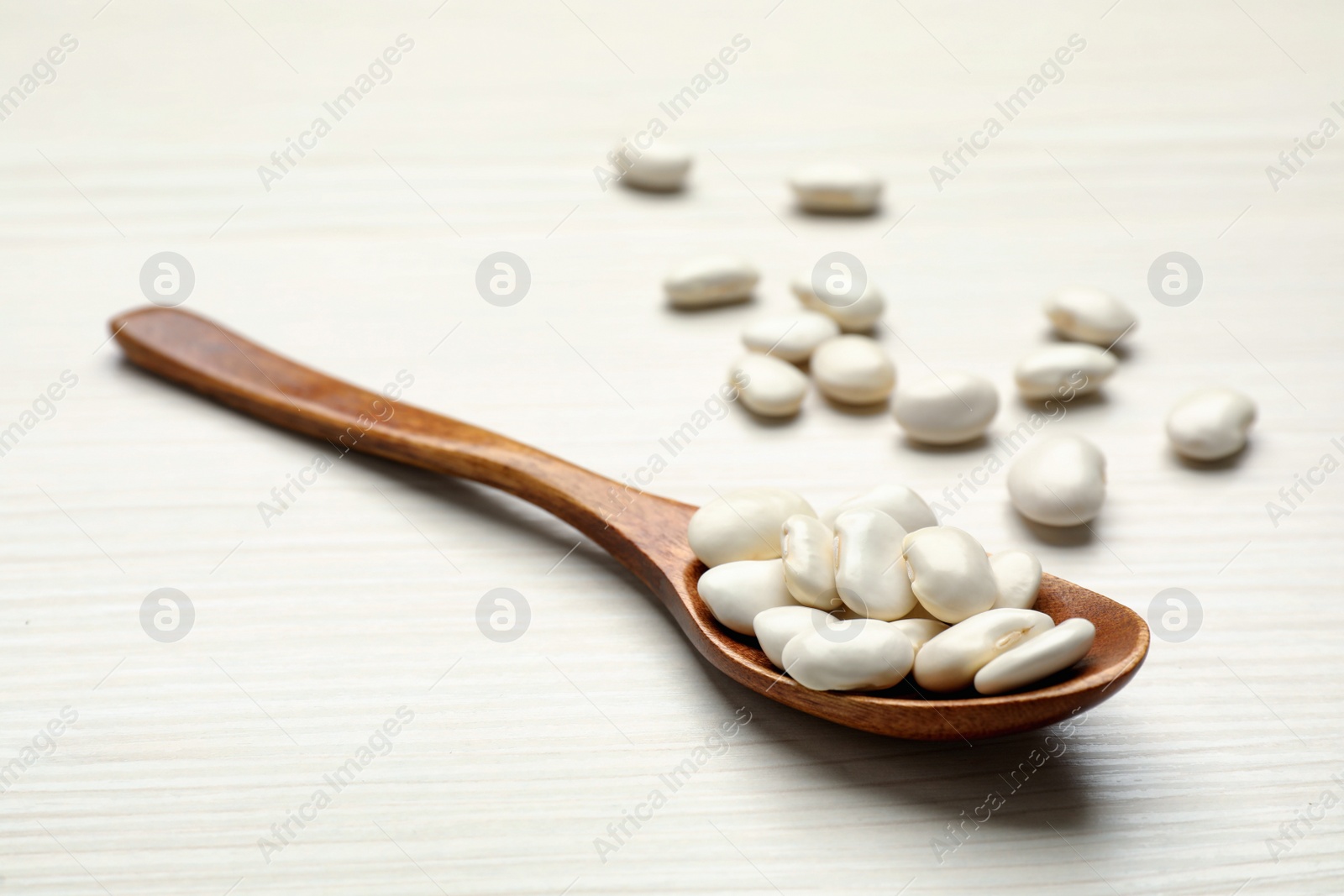 Photo of Raw beans and spoon on white wooden table