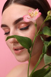 Photo of Beautiful woman with fake freckles and flower on pink background, closeup