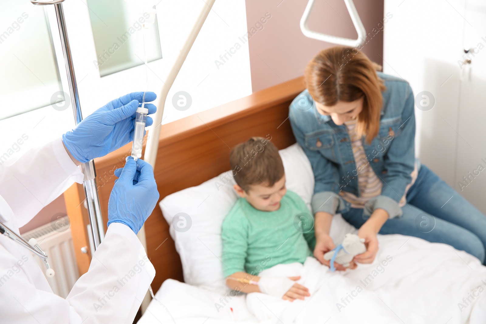 Photo of Doctor adjusting intravenous drip for little child in hospital during parent's visit