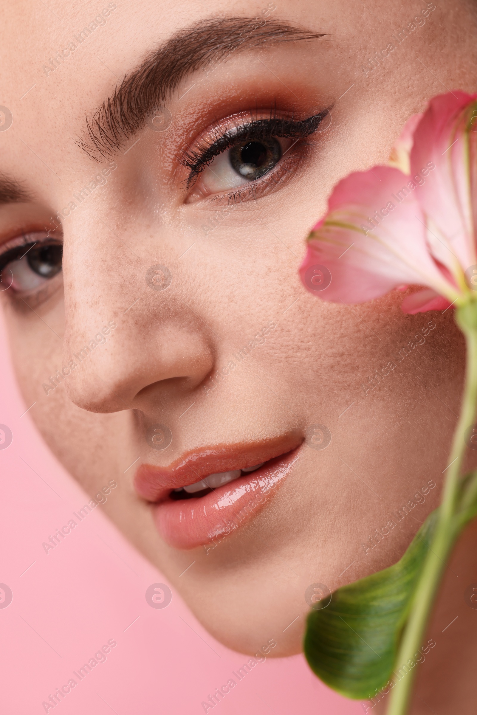 Photo of Beautiful woman with fake freckles and flower on pink background, closeup