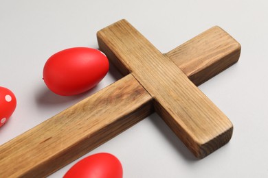 Wooden cross and painted Easter eggs on light grey background, closeup