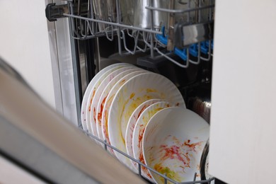 Photo of Open modern dishwasher with dirty tableware in kitchen